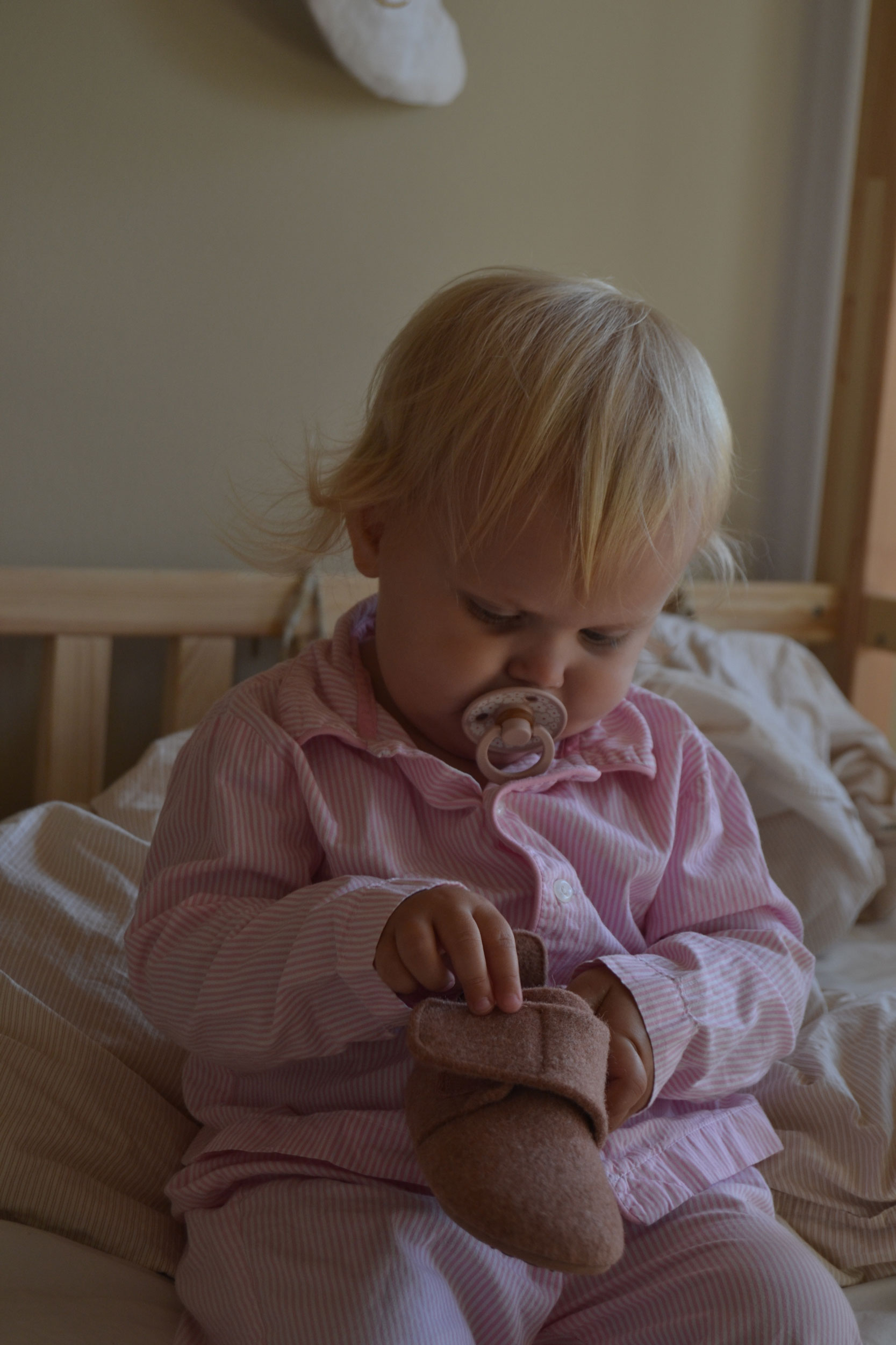 En pige sidder i nattøj med en Bisgaard sutsko i hånden