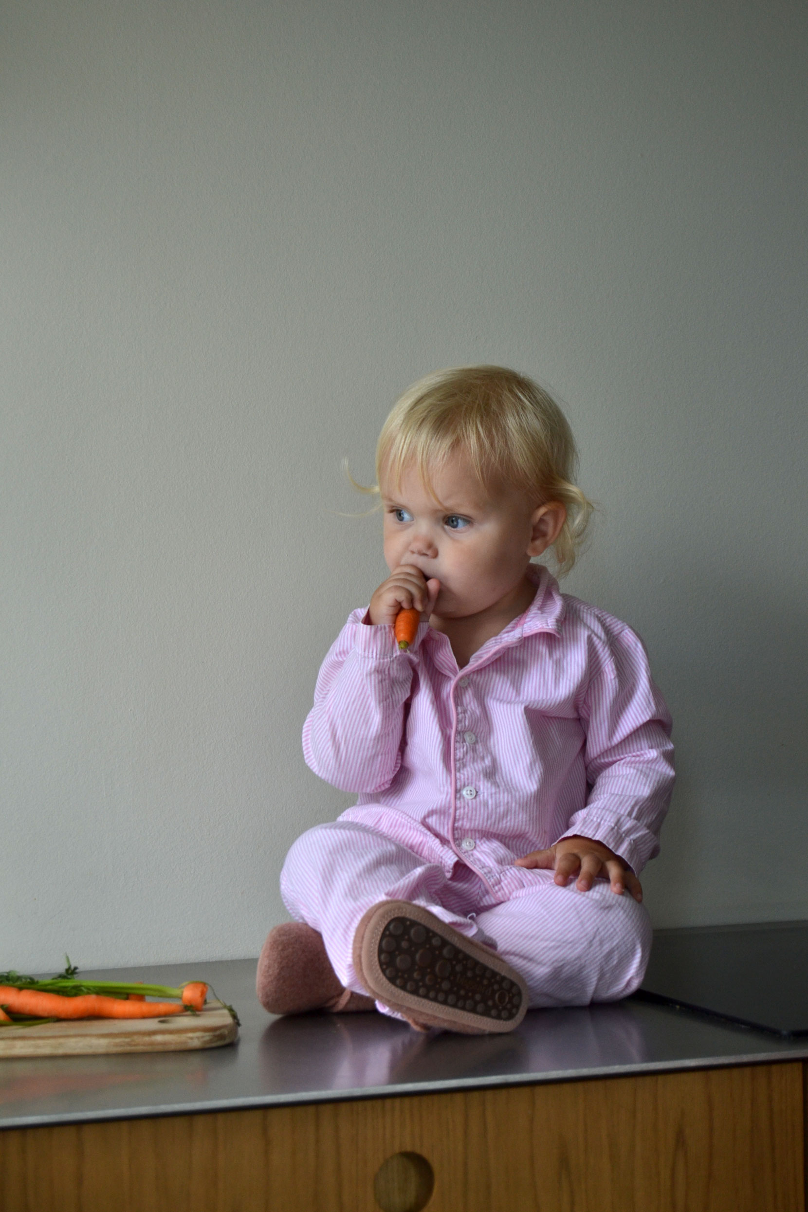 Pige sidder på et køkkenbord med Bisgaard sko på og spiser en gullerod