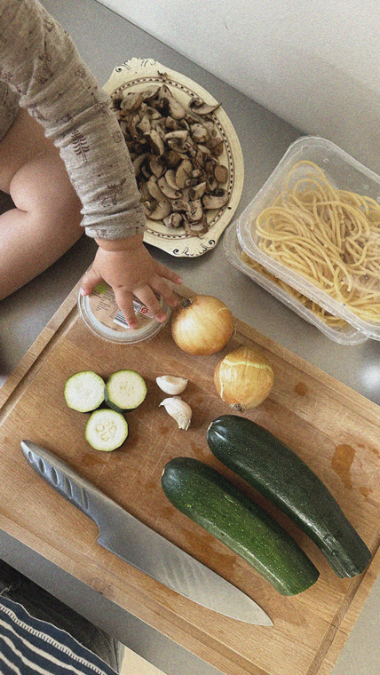Barnehånd rækker ind efter nogle grøntsager på et køkkenbord
